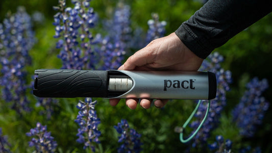 Person holding a PACT Lite Bathroom Kit in front of a field of wildflowers